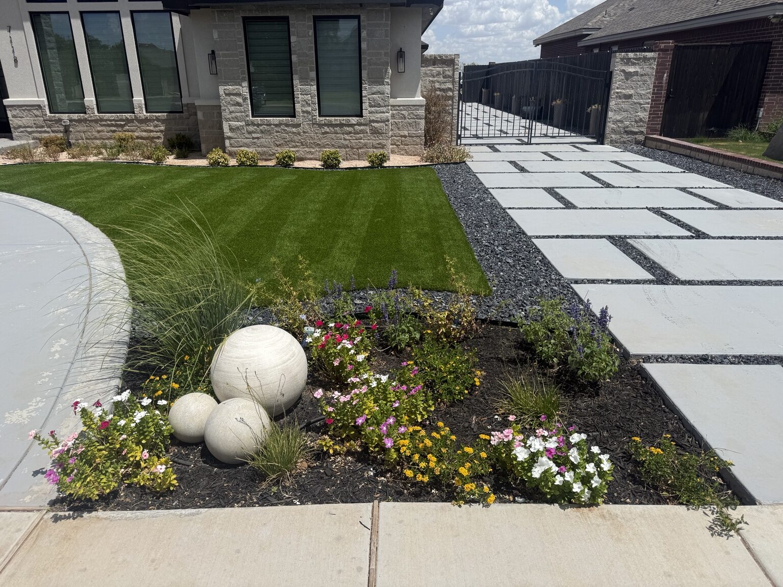 Completed front yard with green turf, flower bed, decorative rock, and concrete driveway