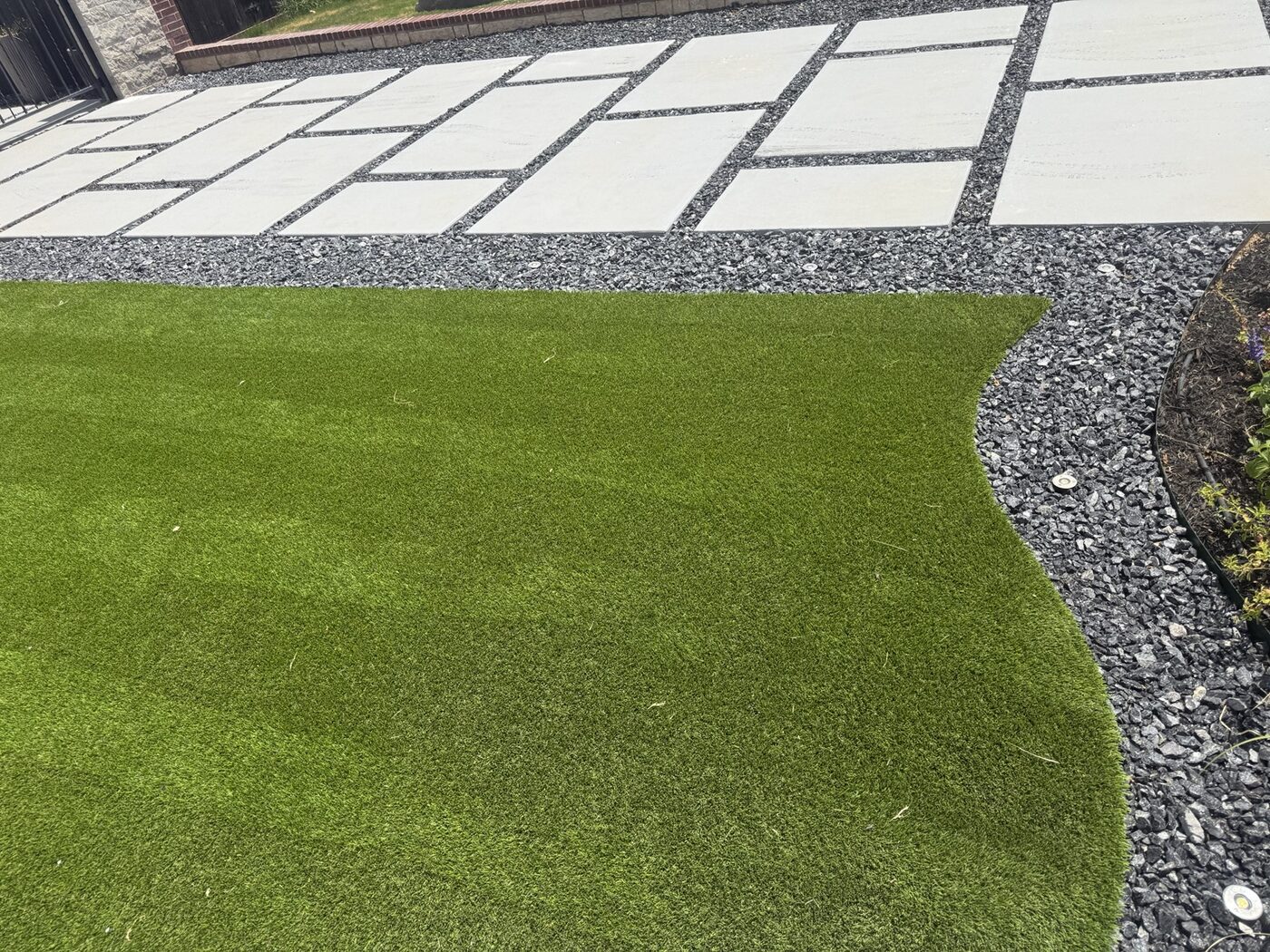 Artificial turf next to modern concrete pads and black decorative rock